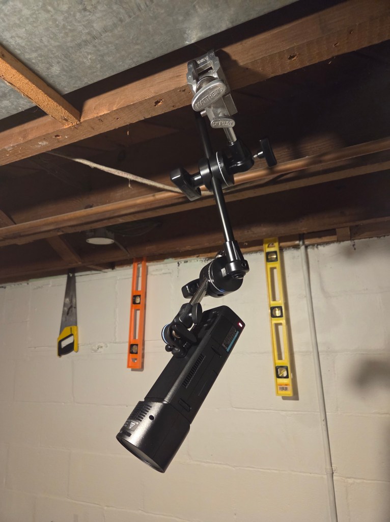 A flash hangs from the ceiling mounted on an arm in a basement.